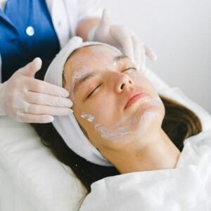 Crop beautician massaging client face with lotion during spa procedures