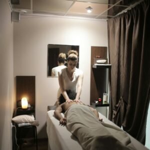 Professional masseuse in white uniform massaging shoulders and neck of relaxed female client while working in comfortable modern salon